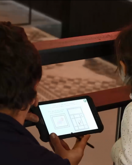 Un enfant et un adulte utilisent la tablette Arkéofil.